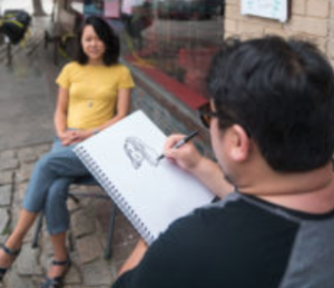 Photo of Paul Choi and friend drawing portraits on the streets of Asheville Made magazine